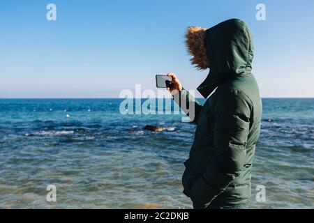 Junger Mann ein Bild von der Marine auf dem Smartphone, im Freien. Ansicht von hinten. Stockfoto
