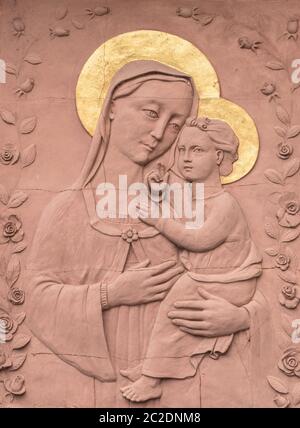 Skulptur in Flachrelief in roten Stein von Maria und Jesuskind, mit goldenen Kronen. Ideal für Konzepte, Ereignisse und Hintergründe. Stockfoto