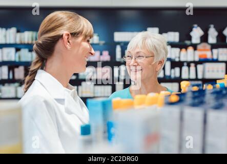 Chemiker und Kunde stehen in der Apotheke zwischen den Regalen und reden Stockfoto
