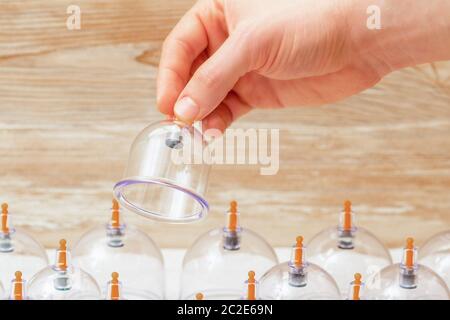 Hand des Massagegeräts hält Vakuumglas Tasse über Satz Gläser auf dem Tisch in Spa. Stockfoto