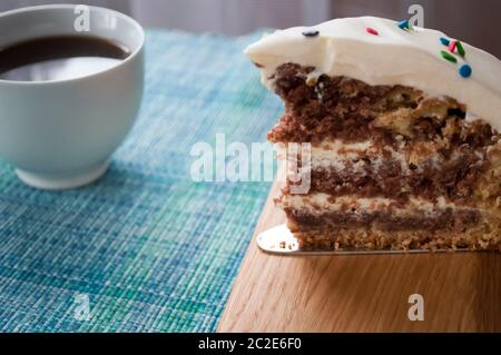 Ein Stück Schokoladenkuchen mit Sahne auf und eine Tasse Kaffee aus der Nähe mit bunten Belag dekoriert Stockfoto