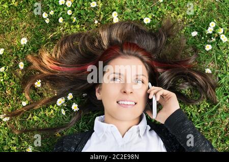 Meine Gedanken und Wünsche mit Ihnen. Nahaufnahme von einem schönen jungen Mädchen liegt auf grünem Gras mit Hören ausgebreitet, am Telefon zu sprechen. Stockfoto