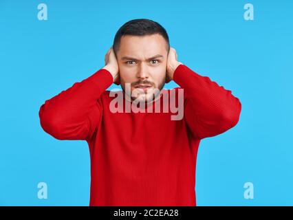 Ein hübscher Mann, der seine Ohren mit Händen bedeckt, die Angst haben, schlechte Nachrichten zu hören Stockfoto