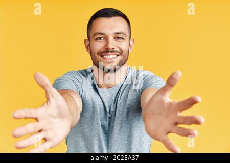 Schöner glücklicher Mann mit offener Hand bereit für Umarmungen auf gelbem Hintergrund Stockfoto