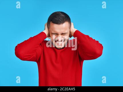 Ein hübscher Mann, der seine Ohren mit Händen bedeckt, die Angst haben, schlechte Nachrichten zu hören Stockfoto