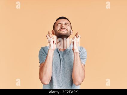 Junger Mann macht einen Wunsch und bitten um Glück mit gekreuzten Fingern isoliert auf gelbem Hintergrund Stockfoto