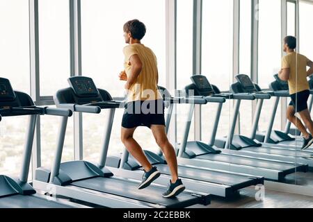 Ganzkörperportrait des jungen Sportmanns, der im Fitnessstudio auf einem Laufband läuft Stockfoto