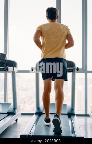 Ganzkörperportrait des jungen Sportmanns, der im Fitnessstudio auf einem Laufband läuft Stockfoto