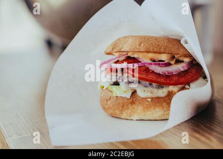 Köstliche frische hausgemachte Käse Burger mit gegrilltem Fleisch, Käse, Tomaten, Salat und Zwiebelringe in Kraftpapier. Stockfoto