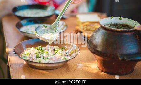 Okroshka - Russische Kalte Suppe. Eine Frau gießt Suppe auf Teller, steht an der frischen Luft. Stockfoto