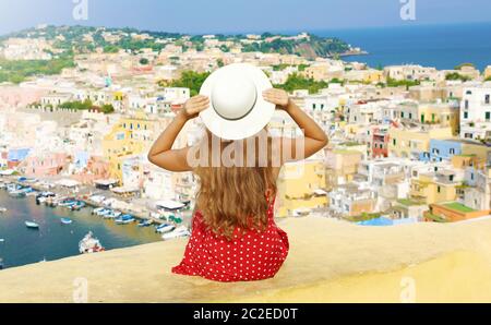 Schöne junge Frau mit Hut sitzen auf Wand bei herrlichem Panoramablick auf die Insel Procida, Neapel, Italien. Stockfoto