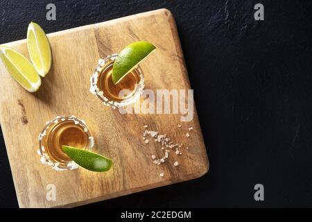 Goldene Tequila-Aufnahmen mit Salz- und Limettenscheiben, oben auf Schwarz Stockfoto