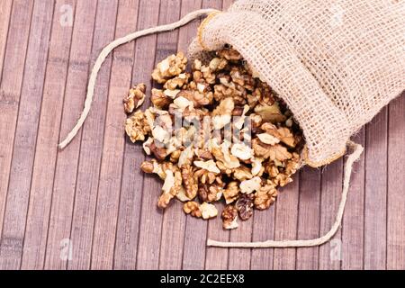 Nahaufnahme von Walnüsse in sackleinen Sack auf einer hölzernen Hintergrund verschüttet. Stockfoto