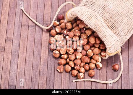 Nahaufnahme von Haselnüssen in einem sackleinen Sack auf Holz- Hintergrund verschüttet. Stockfoto