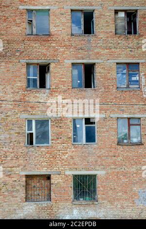 Altes Backsteingebäude aus der Zeit der UdSSR. Sowjetische Architektur. Eine einstürzende Ziegelwand mit kaputten und offenen Fenstern. Ein echtes Wohnviertel Stockfoto