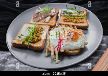 Verschiedene Sandwiches zum Frühstück, Snack, Vorspeisen mit Spiegelei, Erdnusspaste, Erbse Microgreen. Flach liegend, Draufsicht. darl Hintergrund. Schnell gesund Stockfoto