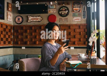 Frau überprüft ihr Handy, während sie Kaffee, Chill-Konzept Stockfoto