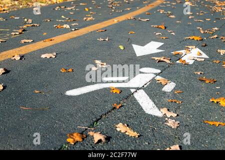 Lackiertes weißes Fußgänger-Symbol mit Pfeil auf Asphaltstraße an der Stadtstraße oder Park am Herbsttag. Spezielles Konzept für die markierte Strecke. Schließen Stockfoto