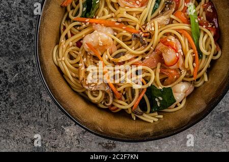 Brate Nudeln mit Gemüse und Garnelen in schwarzer Schüssel rühren. Hintergrund aus Schiefer. Draufsicht. Stockfoto