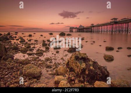 Llandudno Pier bei Sonnenuntergang mit einem glatten Meer und Felsen. Nordwales Touristenziel für Ferien Stockfoto