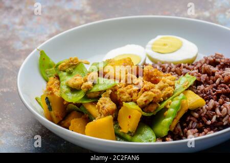 Pfannengerichte Zuckerschoten mit Kürbis und Huhn, serviert mit braunem Reis und gekochtem Ei Stockfoto