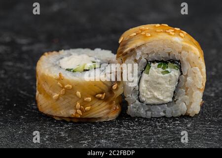 Köstliche Brötchen mit Thunfisch, Avocado, Käse, Kaviar und Aal werden auf einen schwarzen Steinteller gelegt und mit Sojasauce überzogen Stockfoto