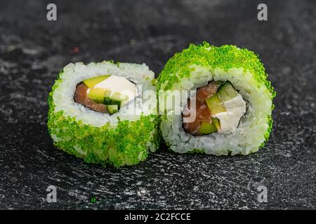 Sushi-Brötchen mit Tobiko Green Caviar, Frischkäse und Fisch auf schwarzem Holztisch Hintergrund Stockfoto