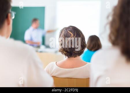Lehrer an der Universität vor einer Tafel angezeigt. Die Schüler hören Vortrag und Notizen zu machen. Konzentrieren Sie sich auf die Schüler. Stockfoto