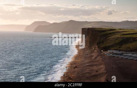 Die Leute laufen am Strand von Burton Freshwater entlang, unter den Sandstein-Ostklippen von West Bay in der Nähe von Bridport an Dorset's Jurassic Coast. Stockfoto