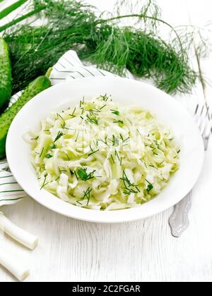 Salat von frischen Kohl, grüne Zwiebeln und Gurken mit Essig und Pflanzenöl Dressing in einer Platte, Handtuch, Dill und Gabel auf Holzbrett Hintergrund Stockfoto