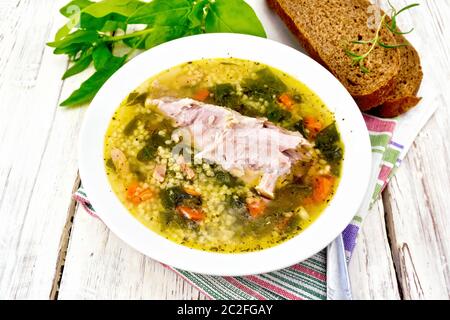 Schweinerippchen Suppe mit Couscous und Spinat in einer Platte auf eine Serviette, Brot auf dem Hintergrund einer Holzplatte Stockfoto