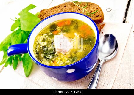 Schweinerippchen Suppe mit Couscous und Spinat in einer blauen Schale auf der Serviette, Brot auf Holzbrett Hintergrund Stockfoto