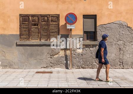 Mann in Shorts und T-Shirt mit Gesichtsmaske geht vorbei an alten notleidenden Fassade eines Gebäudes in El Medano, Teneriffa, Kanarische Inseln, Spanien Stockfoto