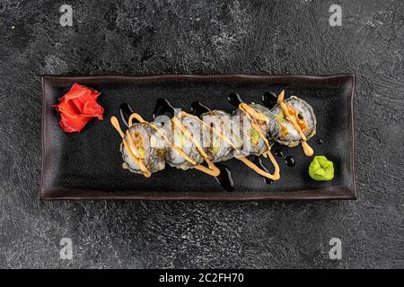 Gebackene Sushi-Brötchen mit Wasabi und Ingwer auf schwarzem Hintergrund. Japanische orientalische Küche Stockfoto