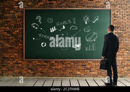 Geschäftsmann suchen und denken vor einer Tafel Backstein Wand mit der Entwicklung Grafik-Strategie . Business Metapher der Lösung Konzept . Stockfoto