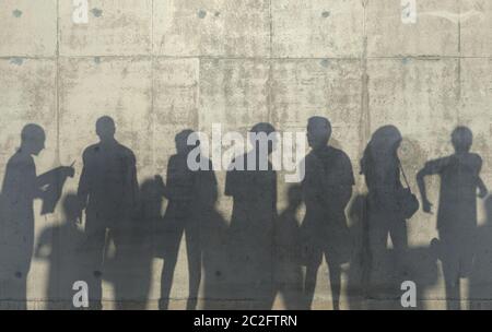 Eine Gruppe von Menschen, die in entspannter Pose gehen, wirft einen Schatten auf die Betonwand. Konzeptionelle kreative Illustration mit Silhouetten von Männern und Frauen. Kopieren Stockfoto