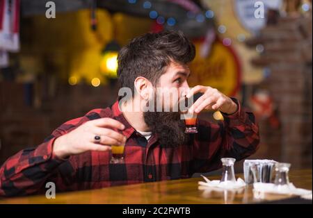 Betrunkene Konzept. Hipster hält Glas mit alkoholischem Getränk, kurzen Cocktail. Kerl verbringen Freizeit in der Bar trinken Cocktail, entkokettes Hintergrund. Mann mit fröhlichem Gesicht sitzt allein an der Theke. Stockfoto