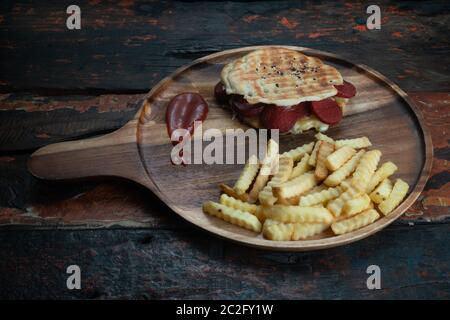 Gegrilltes Panini-Sandwich mit türkischen Würstchen und Käse, serviert mit frischen knusprigen pommes frites auf rustikalem Küchentisch aus Holz Stockfoto