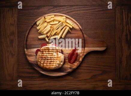 Gegrilltes Panini-Sandwich mit türkischer Wurst und Käse, serviert mit frischen knusprigen pommes frites auf einem Küchentisch aus Holz Stockfoto