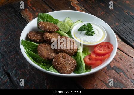 Falafel, vegan geröstete Kichererbsen-Patties mit Knoblauch-Joghurt-Sauce auf rustikalem Holztisch isoliert Stockfoto