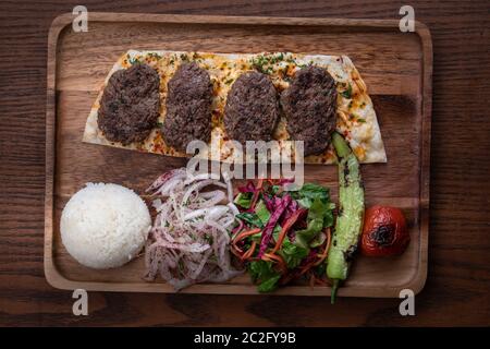 Türkischer Kofte Kebab mit Reis und Gemüse auf Holztisch isoliert Stockfoto