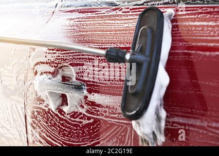 Rotes Auto gewaschen in selbst dienen Autowäsche, Detail auf Pinsel verlassen Striche an Seitentür und Griff Stockfoto