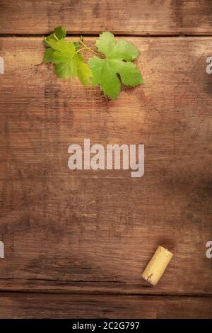 Eine Designvorlage für ein Weinmenü oder eine Weinverkostung Einladung. Ein Weinblatt und ein Weinkorken, von oben auf einem dunklen rustikalen Holz geschossen Stockfoto