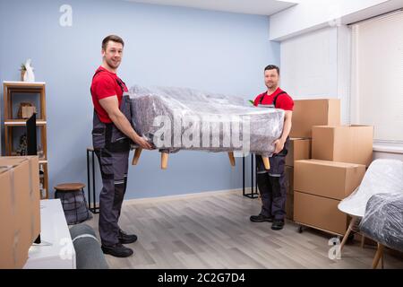 Porträt von zwei jungen Glücklich männlichen Movers Durchführung gewickelt Sofa in neues Haus Stockfoto