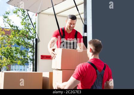 Lächelnden jungen männlichen Mover Entladen in einen Umzugswagen und die Übergabe eines Kartons Stockfoto