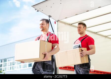 Glückliche junge männliche Movers Holding Kartons stehen In Moving Van Stockfoto