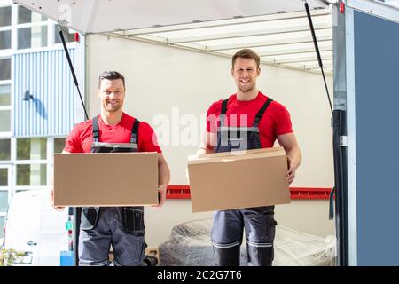 Glückliche junge männliche Movers Holding Kartons stehen In Moving Van Stockfoto