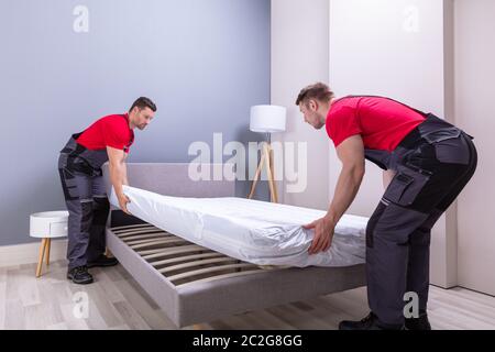 Zwei männliche professionelle Movers in Uniform, die Matratze auf dem Bett in neues Haus Stockfoto