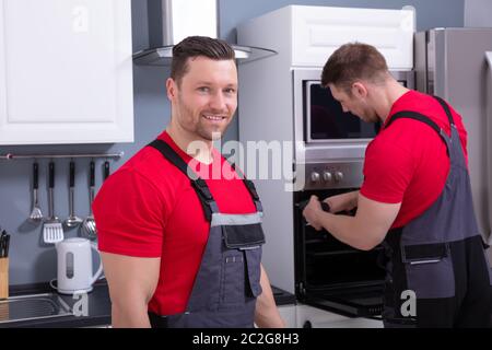 Lächelnden jungen männlichen Techniker mit seiner Assistentin der Instandsetzung der Backofen in der Küche Stockfoto