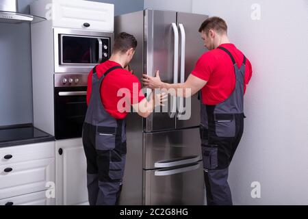 Zwei junge männliche Movers in Uniform, moderne Edelstahl Kühlschrank in der Küche Stockfoto